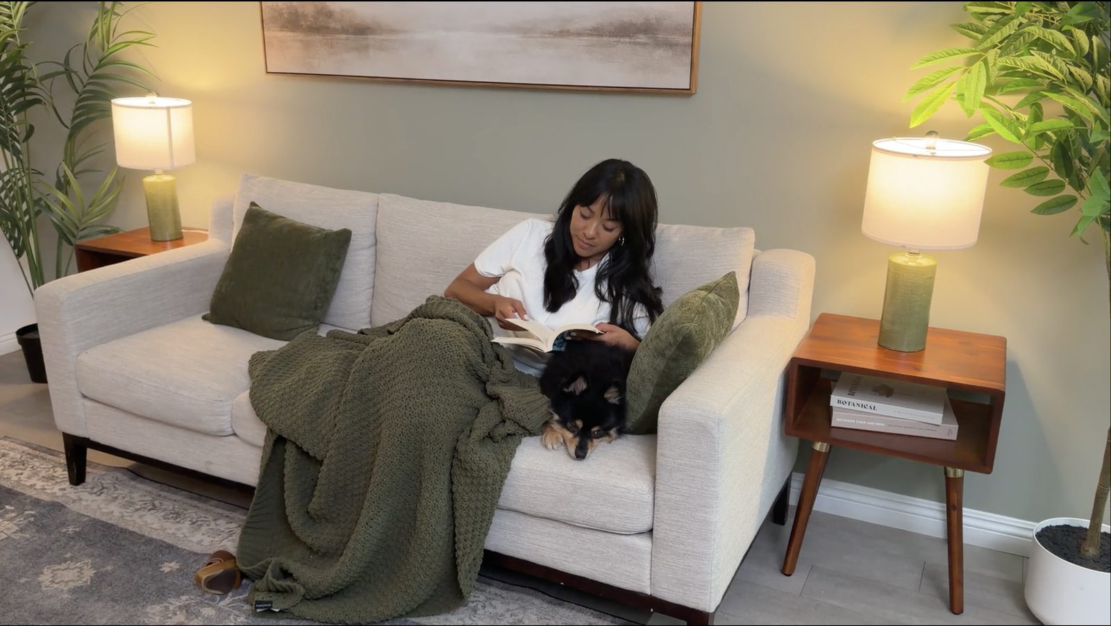 A pet parent reading on the couch with her dog tucked in beside her under a blanket