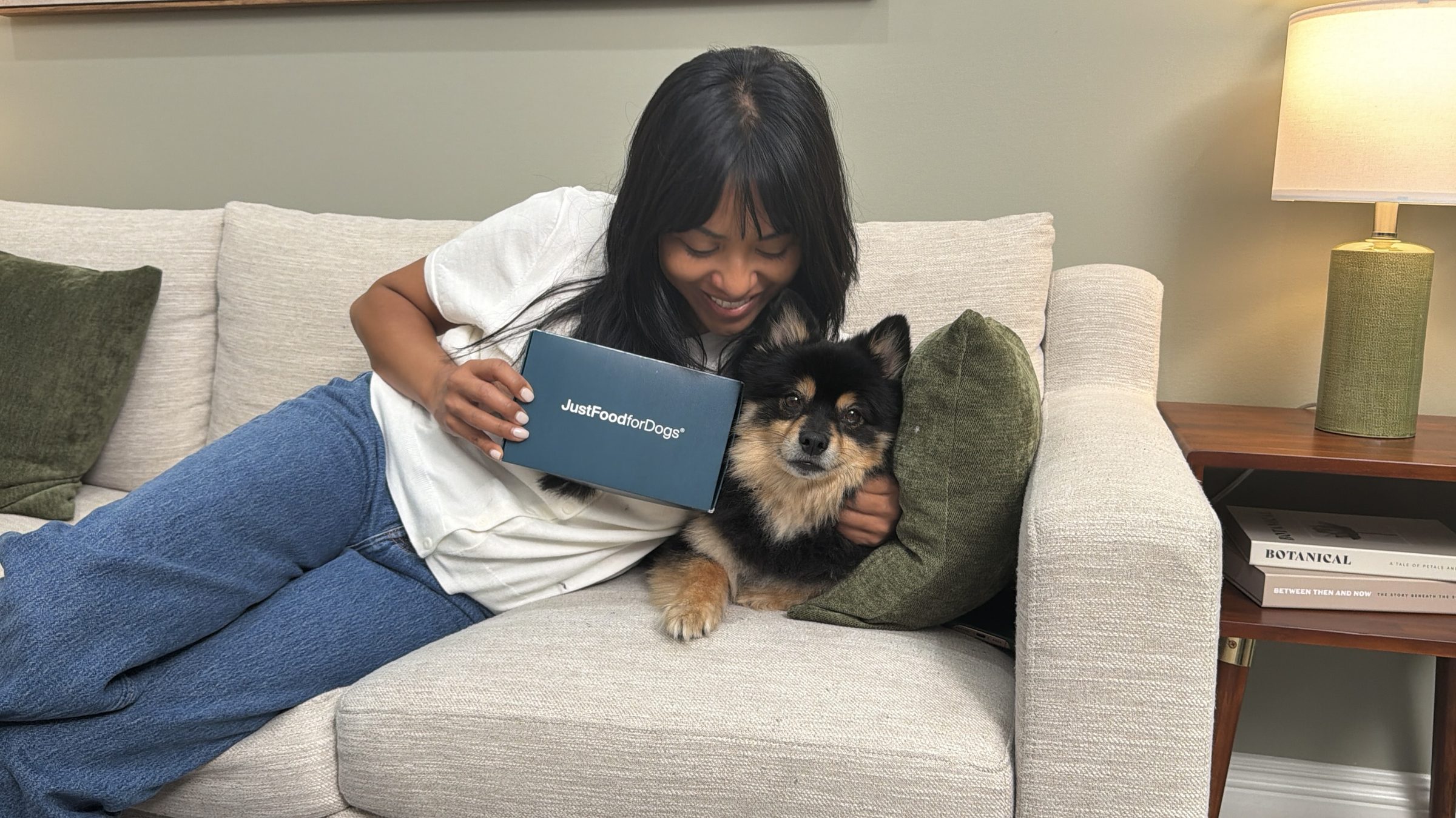 A pet parent snuggled on the couch with her Pomeranian, holding their Biological Age Test kit box